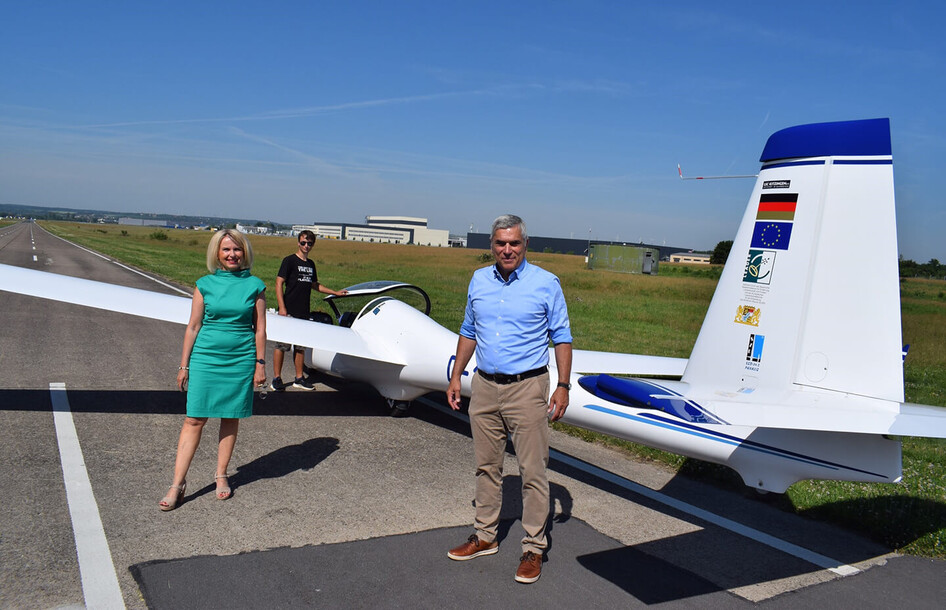 Personen stehen neben einem SZD-54-2 Perkoz Segelflugzeug auf einem Flugplatz.